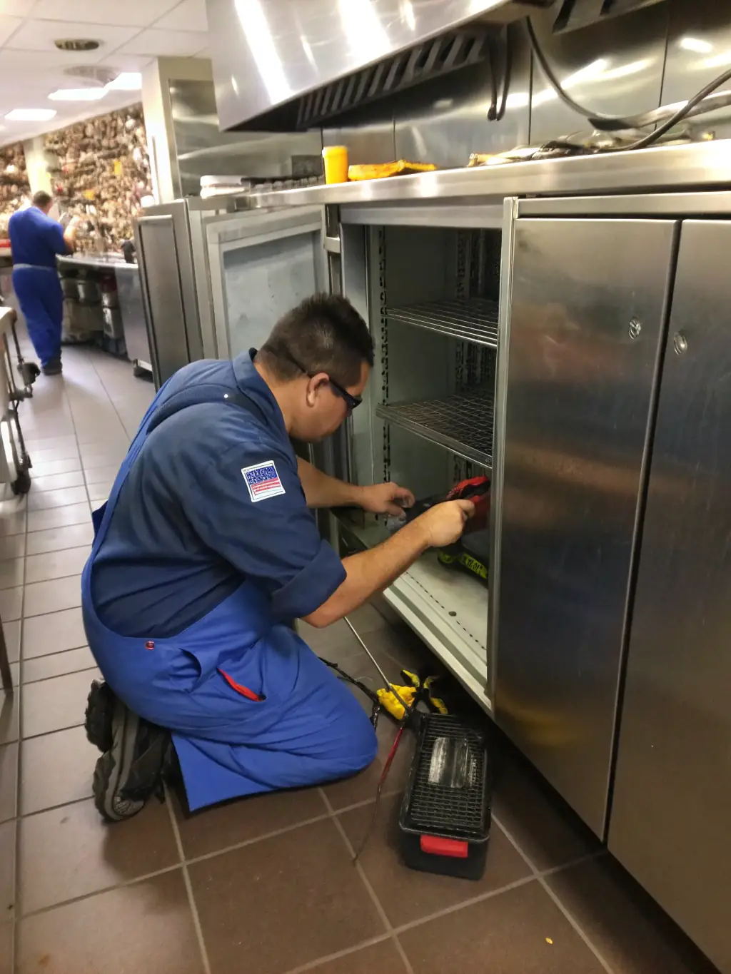 A commercial kitchen with multiple Sub-Zero refrigerators, showcasing a technician working on one of them.